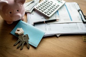 House keys, a piggy bank, a calculator and mortgage paperwork on a desk