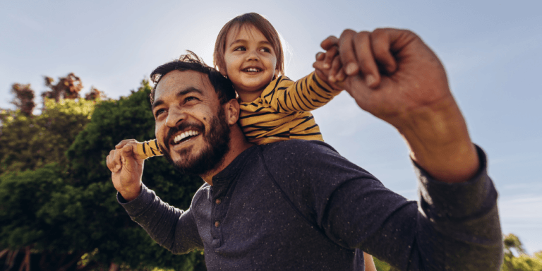 Father carrying his young daughter on his shoulders outdoors